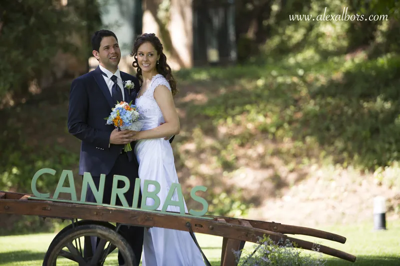 Los novios posan junto a un carro antiguo en un jardín